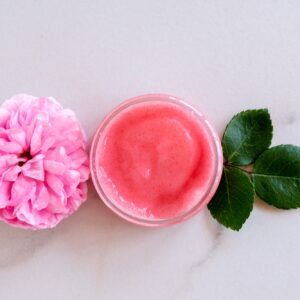 Hygiene bath product. Body, face rose scrub with blooming pink rose flowers on marble background.